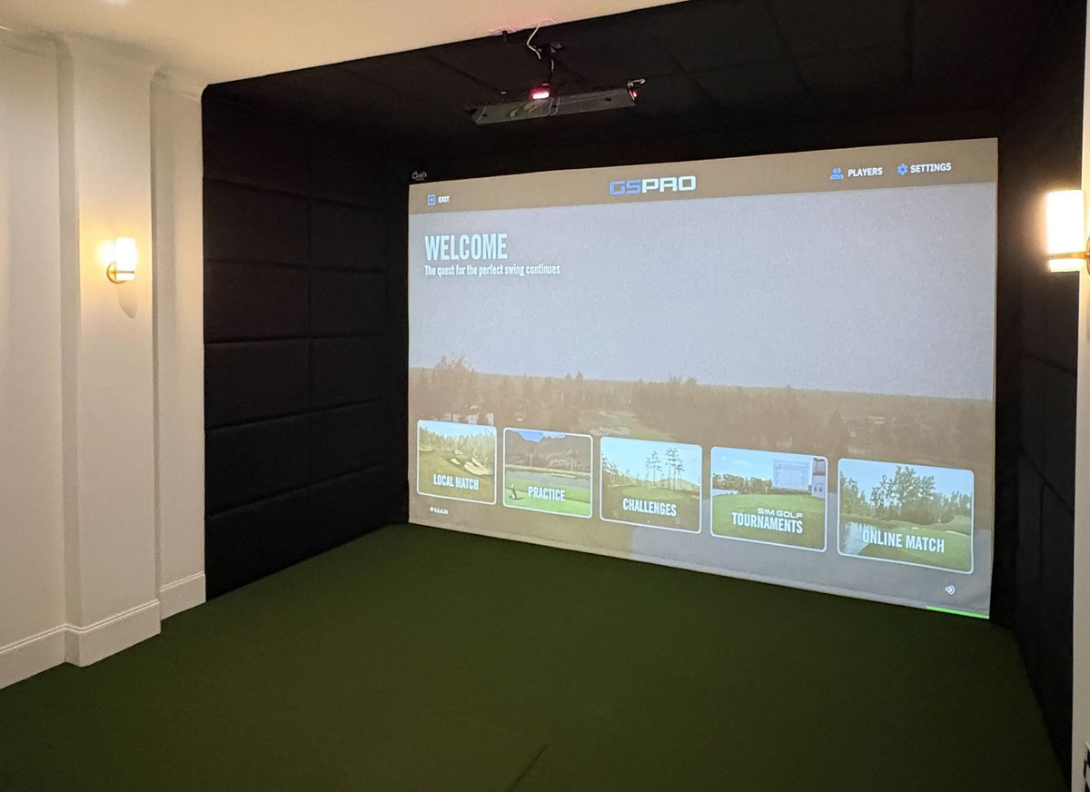 Finished golf simulator bay with a ceiling-mounted projector, padded walls and turf floor