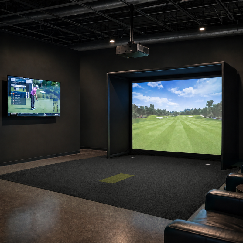 IGO Single-Level Golf Simulator Flooring in black covering a golf simulator bay with the green IGO Local Muni Hitting Strip, lounge seating and a wall-mounted TV.