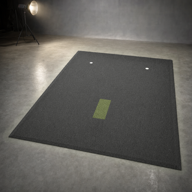IGO Single-Level Golf Simulator Flooring in black with the green IGO Local Muni Hitting Strip and two putting cups, lit by a studio spotlight.