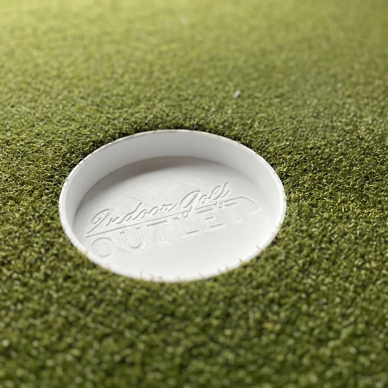 IGO Single-Level Golf Simulator Flooring putting cup sunk in the green turf, embossed with the Indoor Golf Outlet logo.