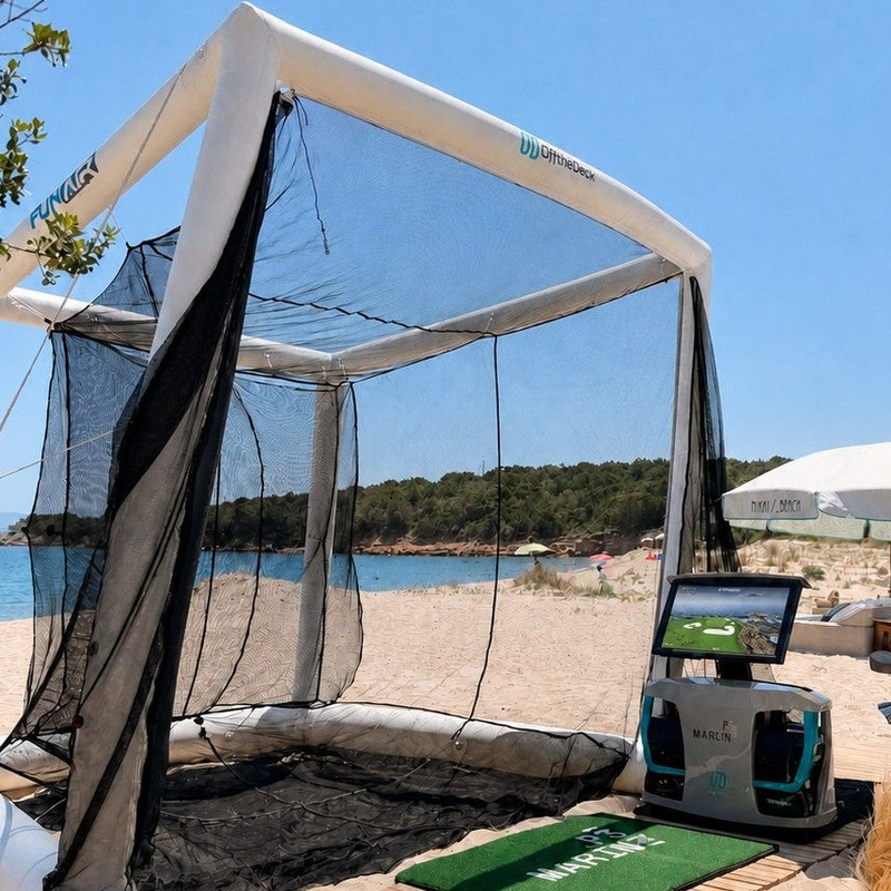 Off the Deck Cube Inflatable Golf Practice Net beach setup with a hitting mat and a portable golf simulator unit beside the net.