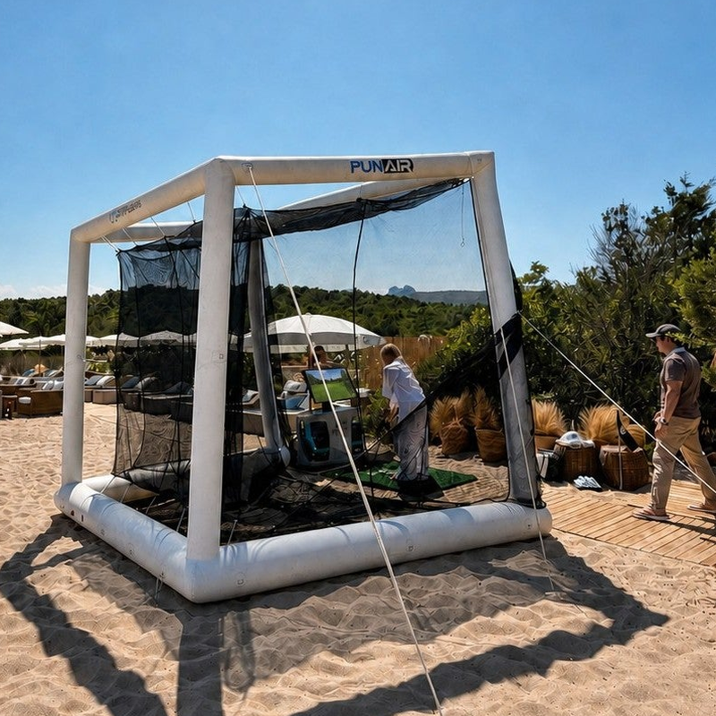 Off the Deck Cube Inflatable Golf Practice Net rear angle on sand showing the anchored guy line and the beach club behind.