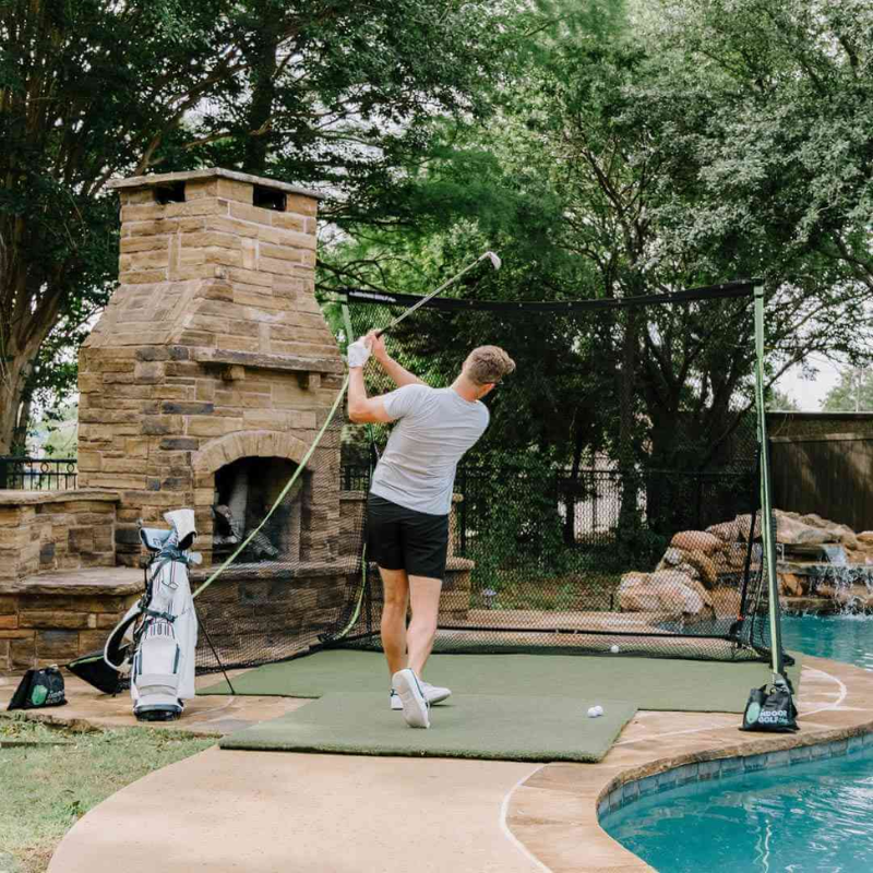 SIGPRO Golf Net with golfer hitting by a fireplace and pool.
