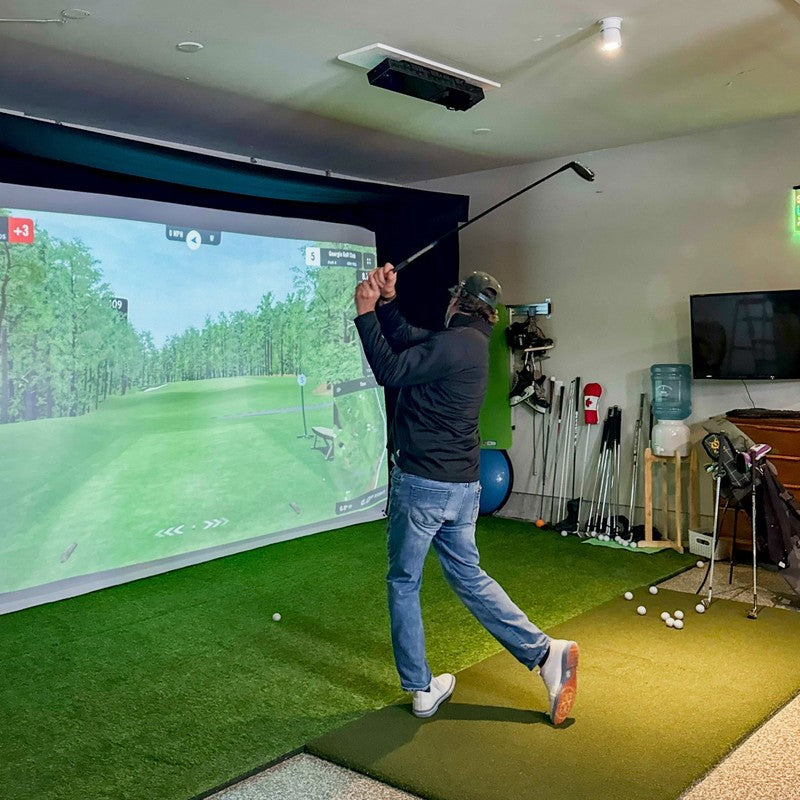 The SportsScreen Vanish LITE Series Golf Simulator Enclosure golfer swinging indoors.