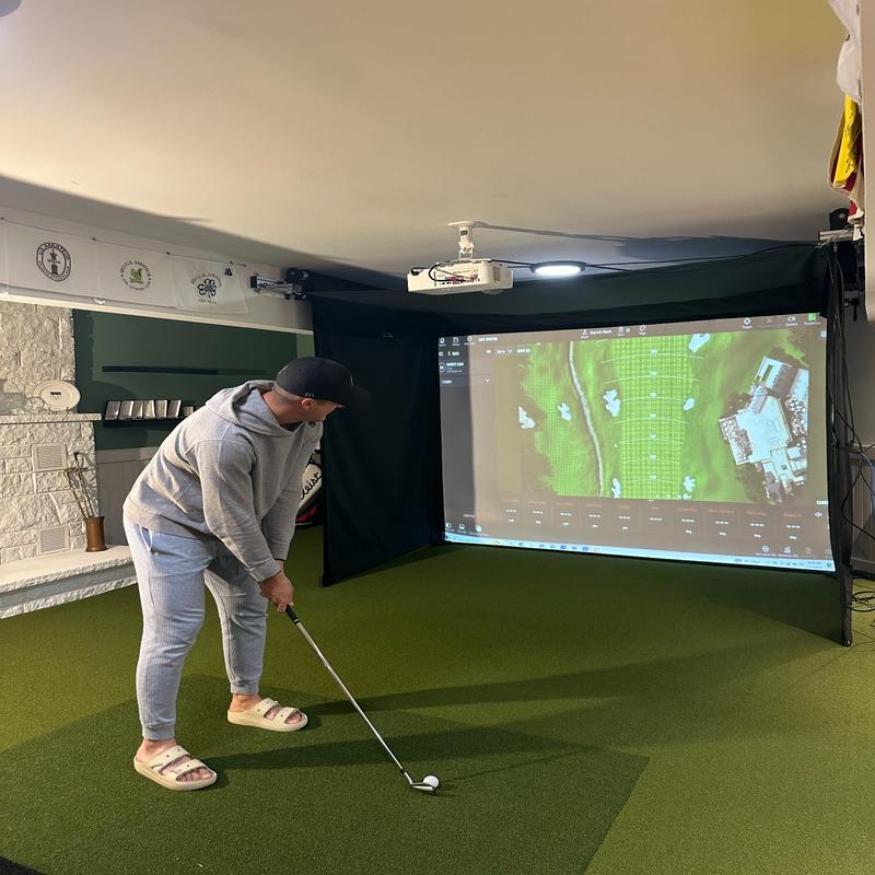 The SportsScreen Vanish Series Golf Simulator Enclosure man teeing up.