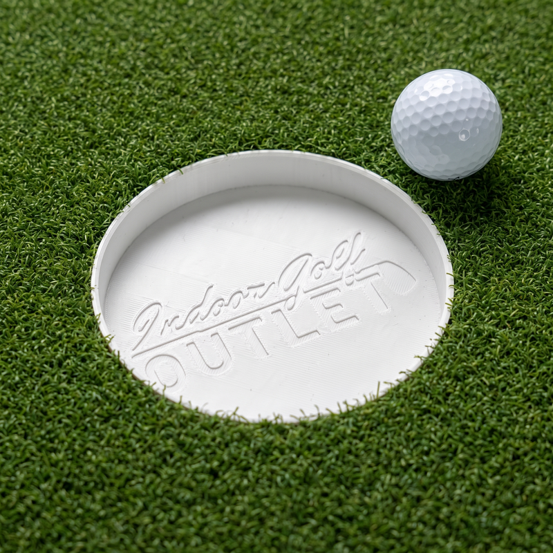 The Indoor Golf Outlet Putting Cup set flush into green putting turf with a golf ball beside it.